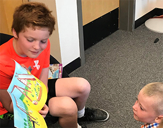 Older student reading book to young student